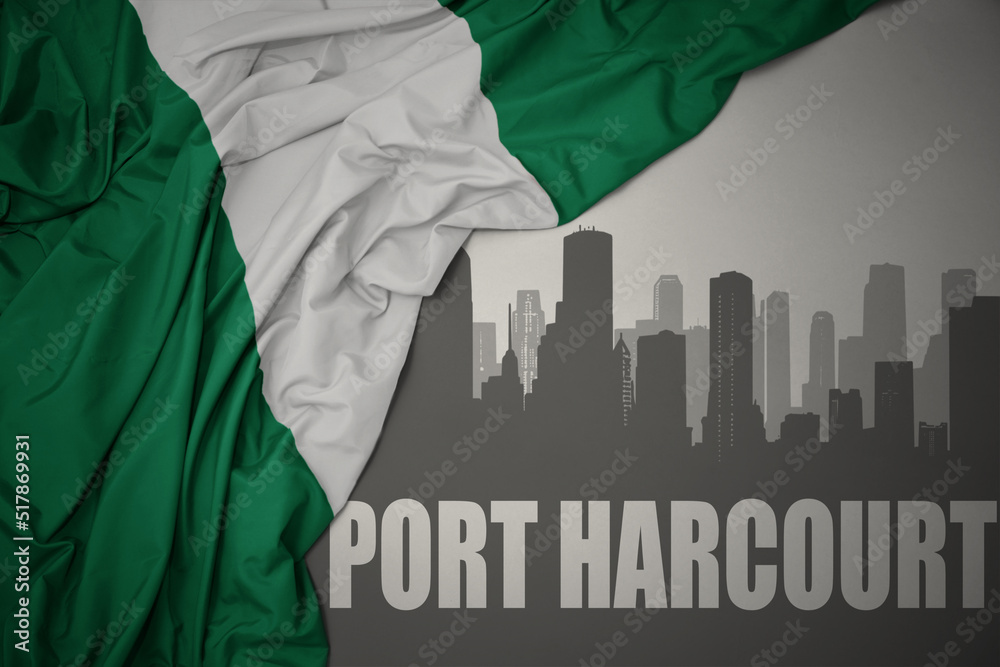 abstract silhouette of the city with text Port Harcourt near waving colorful national flag of nigeria on a gray background.