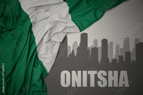 abstract silhouette of the city with text Onitsha near waving colorful national flag of nigeria on a gray background. photo