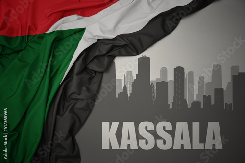abstract silhouette of the city with text Kassala near waving colorful national flag of sudan on a gray background.