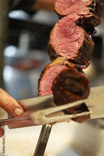 Picanha is a BBQ Steak meat grilled in charcoal. Knife cutting on skewer. Brazilian meat in a Churrascaria restaurant