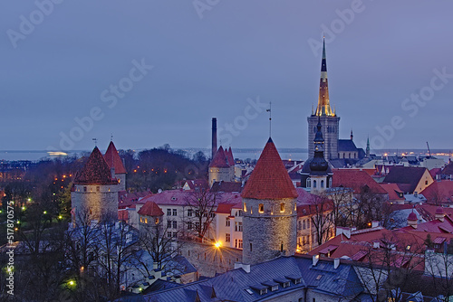 High angle view of downtown Tallinn, showing gothic church towers and medieval city walls and houses with orange tiled roofs in the blue hour