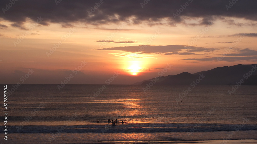 Peaceful seacoast landscape in sunrise time with silhouettes of swimming people near the shore and mountains in the distance . Travelling to the seacoast ,rest near the sea concept.