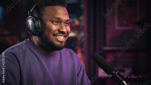 Handsome Young African American Man Talking Into Microphone While Recording Radio Show from His Loft Apartment. Happy Black Male Talking on Camera and Recording Podcast Live on Social Media. photo