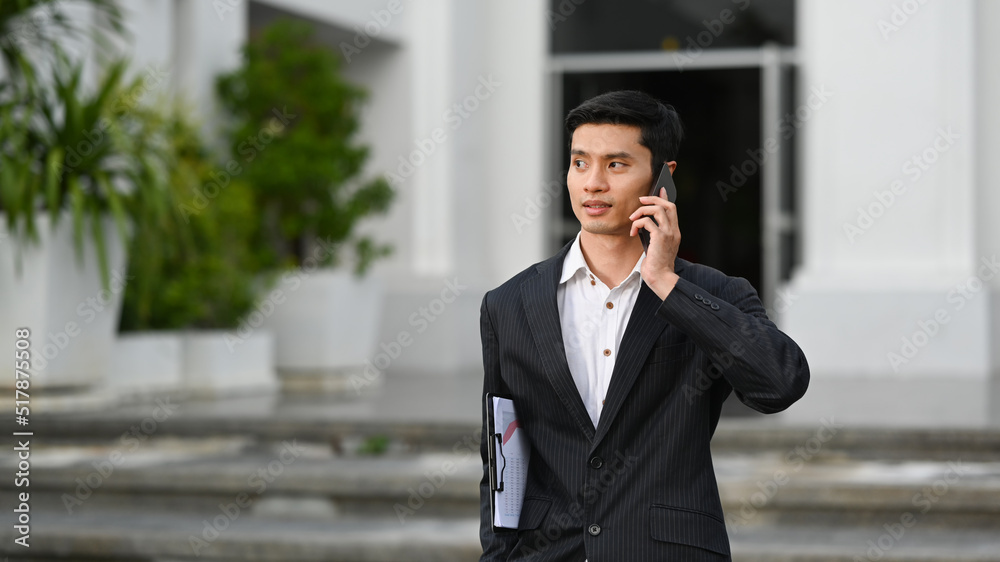 Young businessman in formal clothes standing in front of an office building and talking on mobile phone Young businessman in formal clothes standing in front of an office building and talking on mobile phone