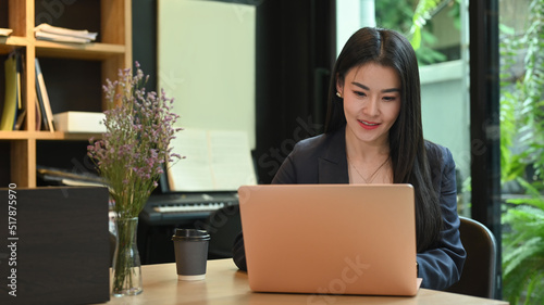 Fotografi Asian woman entrepreneur working, analyzing online information on laptop compute