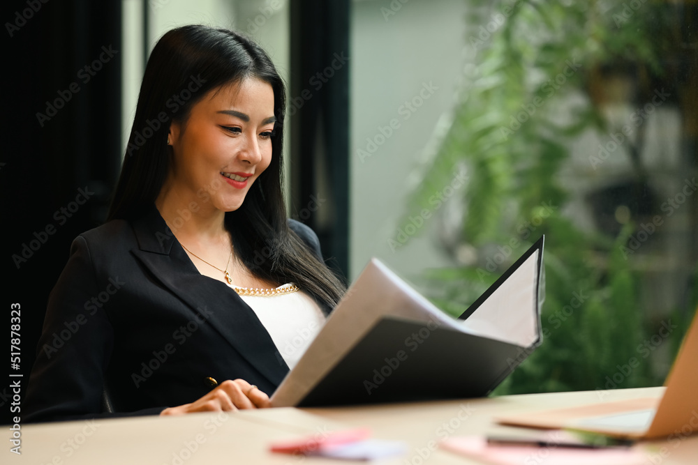 Smiling female manager checking financial report or correspondence at her workplace Smiling female manager checking financial report or correspondence at her workplace