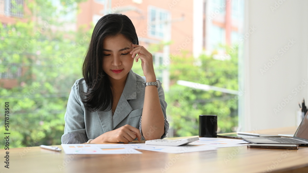Serious businesswoman analyzing marketing research reports at her office desk Serious businesswoman analyzing marketing research reports at her office desk