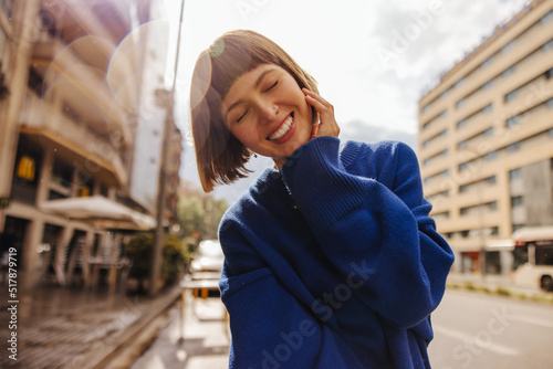 Fotografia Pretty young caucasian woman closing her eyes smiles teeth walking around city