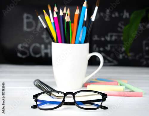 Glasses, a holder with school stationery and a chalkboard in the background. Teacher's Day. Back to school. Close-up. Selective focus.