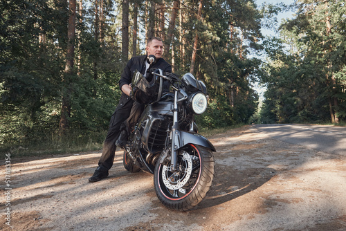 Young male biker travels on a motorcycle alone, stopped on the side of a forest road
