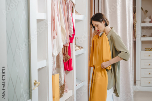 Attractive woman choosing a dress in a dressing room or store. Fashion, style and space organization concept.