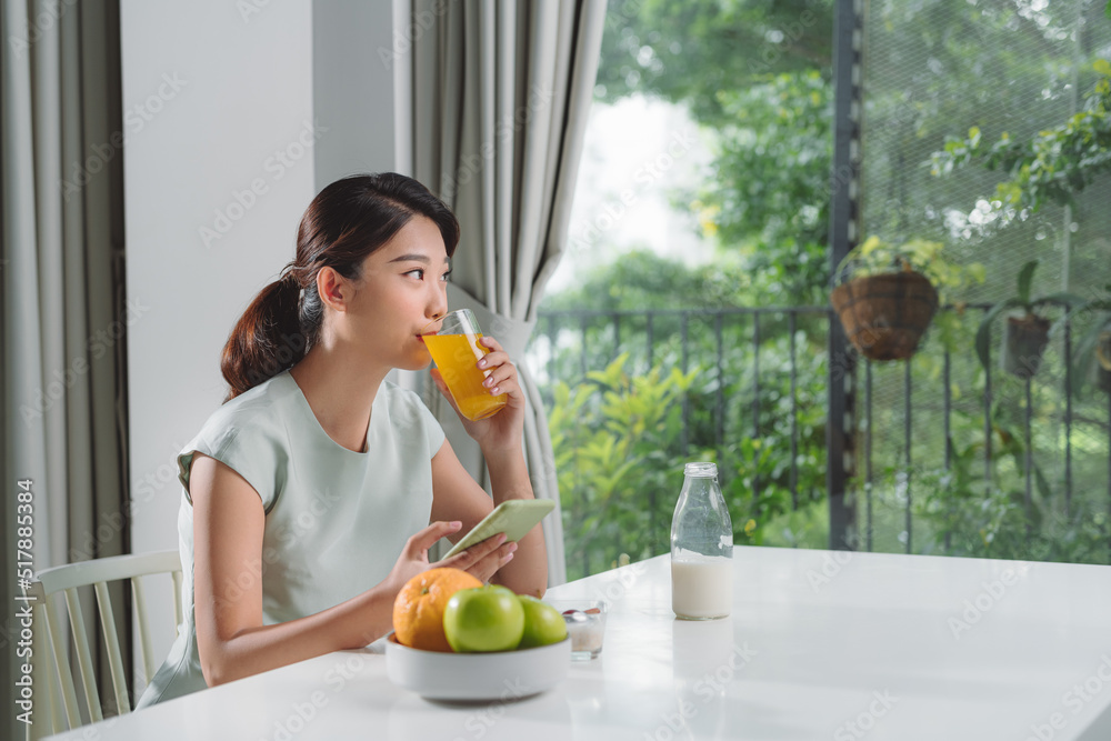 woman having orange juice while using mobile phone at home woman having orange juice while using mobile phone at home