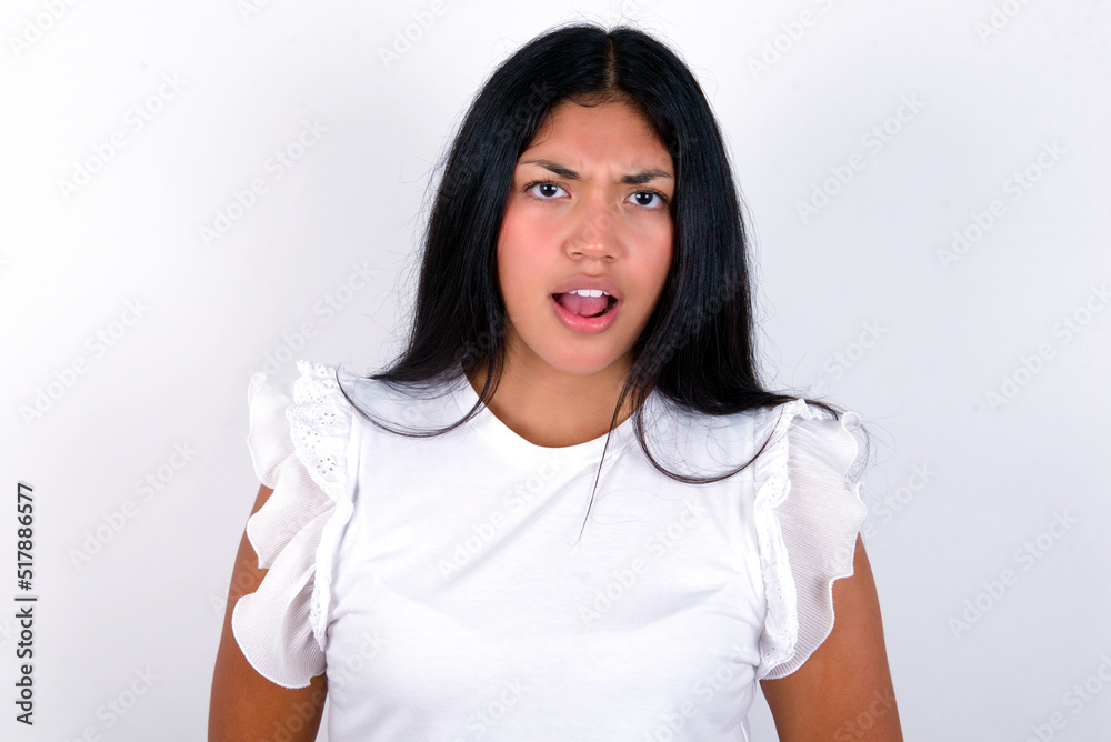 Fototapeta premium Expressive facial expressions. Shocked stupefied young brunette woman wearing white T-shirt standing against white background, keeps jaw dropped feels stunned from what he sees aside.