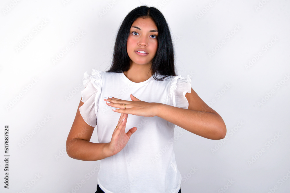 young brunette woman wearing white T-shirt standing against white background feels tired and bored, making a timeout gesture, needs to stop because of work stress, time concept. young brunette woman wearing white T-shirt standing against white background feels tired and bored, making a timeout gesture, needs to stop because of work stress, time concept.