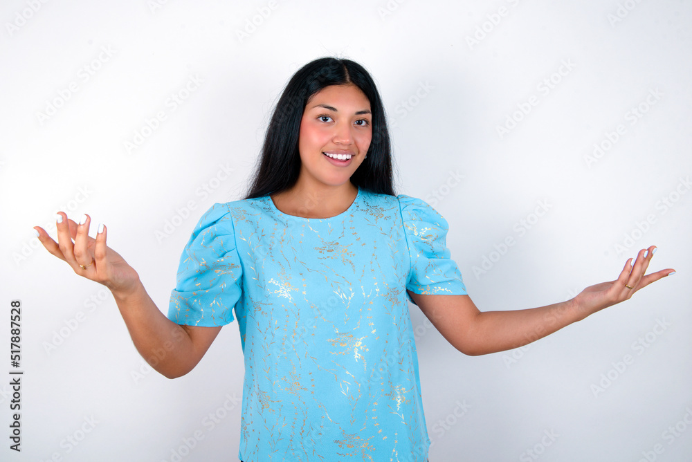 Cheerful young brunette woman wearing blue T-shirt standing against white background making a welcome gesture raising arms over head. Cheerful young brunette woman wearing blue T-shirt standing against white background making a welcome gesture raising arms over head.