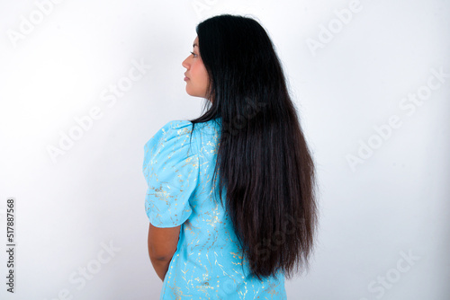 The back view of young brunette woman wearing blue T-shirt standing against white background Studio Shoot.
