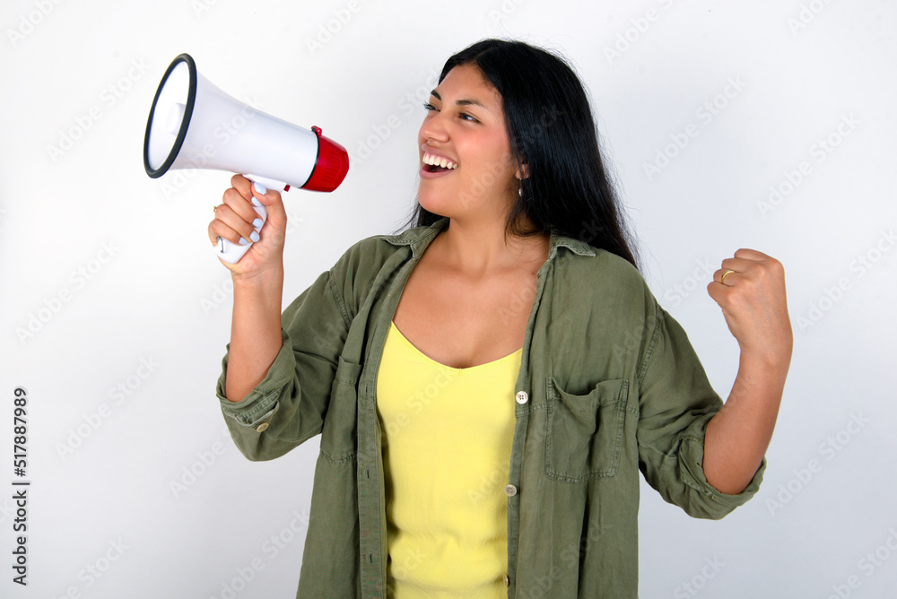 young brunette woman wearing green overshirt standing against white background communicates shouting loud holding a megaphone, expressing success and positive concept, idea for marketing or sales. young brunette woman wearing green overshirt standing against white background communicates shouting loud holding a megaphone, expressing success and positive concept, idea for marketing or sales.
