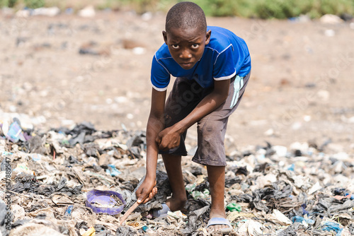 Hungry African boy rummaging through a pile of trash looking for something recyclable or edible  concept of extreme childhood poverty and neglect