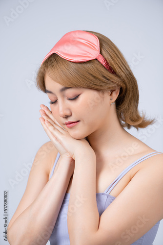 Cheerful asian girl in pajamas standing on white background in sleep mask in morning.