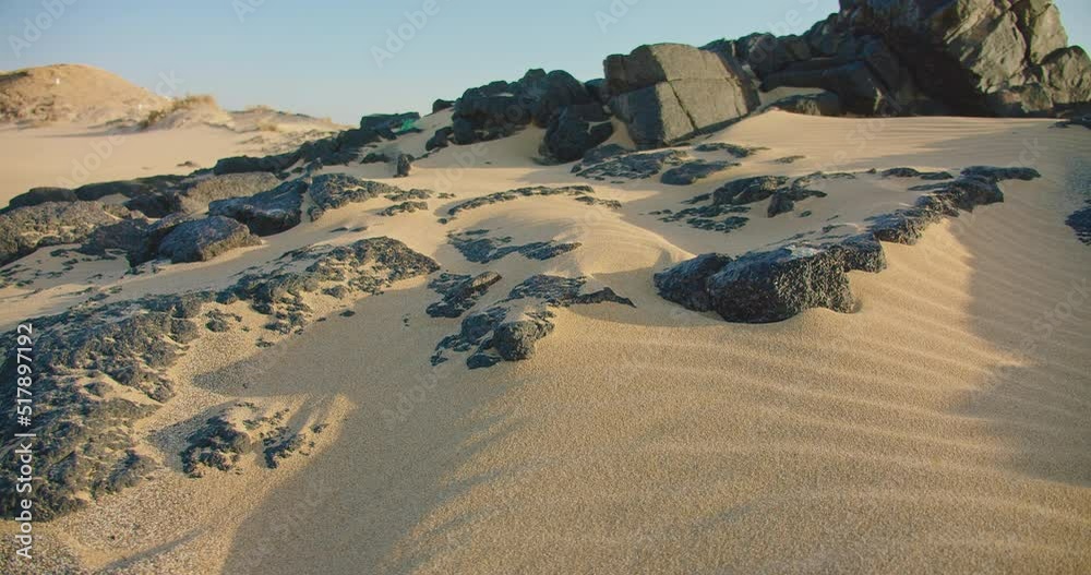 Sandy perfectly clean beach, close-up gusty wind sweeps sand particles along the beach. Sunny day, black stones, 4K real time footage