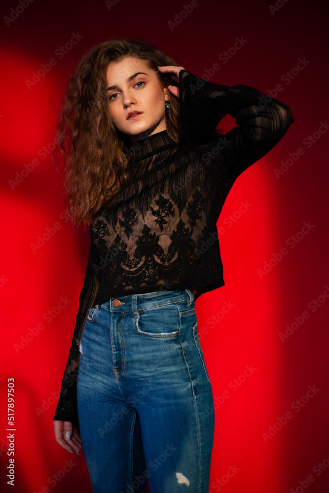 Attractive young woman with makeup and curly hair, dressed in a black blouse and jeans, isolated red background. Attractive young woman with makeup and curly hair, dressed in a black blouse and jeans, isolated red background.