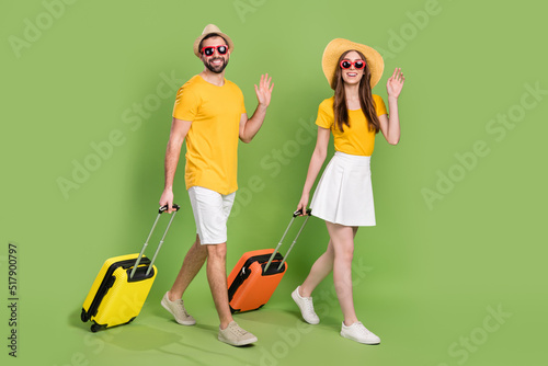 Full length portrait of two people walking arm palm waving hi bye isolated on green color background