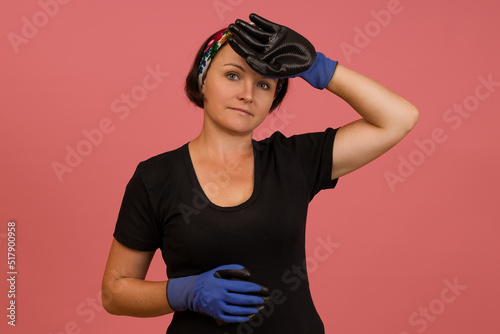 tired woman worker in a t-shirt, gloves and a bandage on her head on a pink background