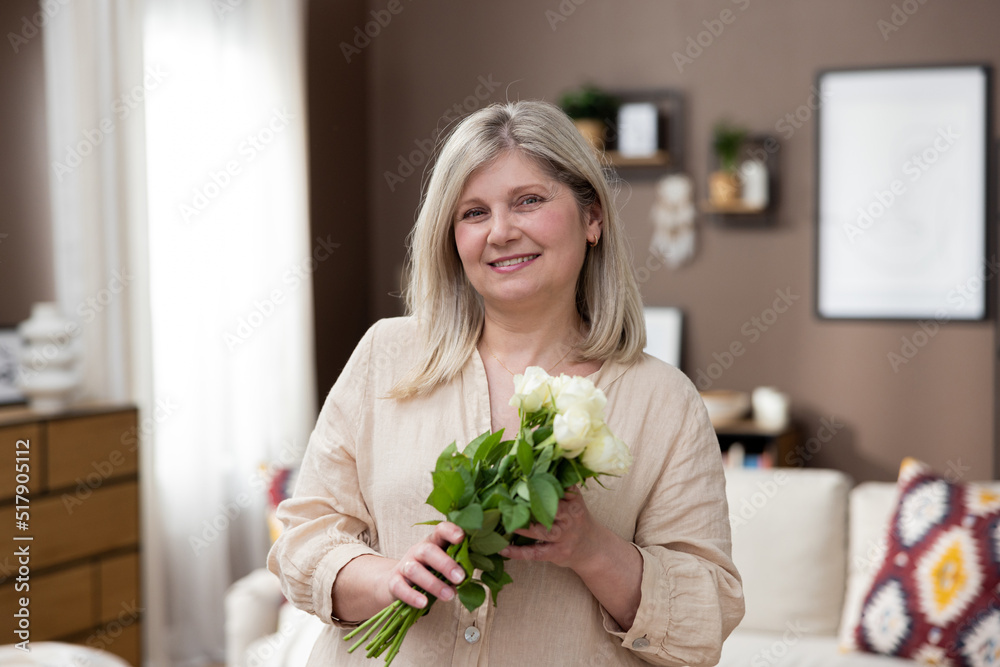 Portrait of old woman relaxing on cozy living room with bunch of flowers in hug. She is looking at camera with happiness. Portrait of old woman relaxing on cozy living room with bunch of flowers in hug. She is looking at camera with happiness.