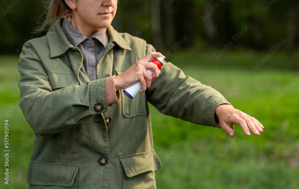 health care, protection and people concept - woman spraying insect repellent or bug spray to her hand at park