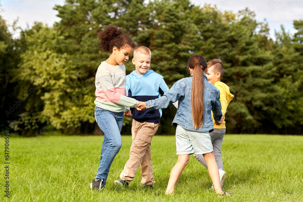 childhood, leisure and people concept - group of happy kids playing round dance at park