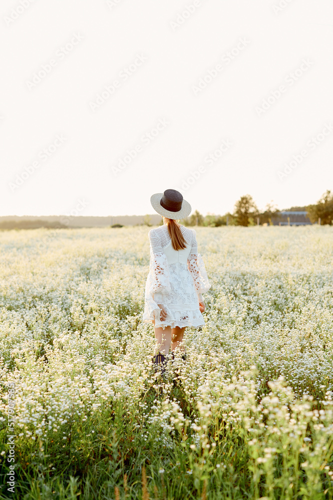 a girl in a hat and light clothes walks through a flowering field