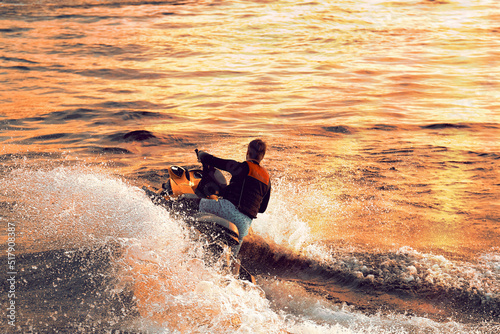 A guy on a jet ski swims at high speed across the sea. A man rides a jet ski in the sun at sunset. Splashes of water in different directions.