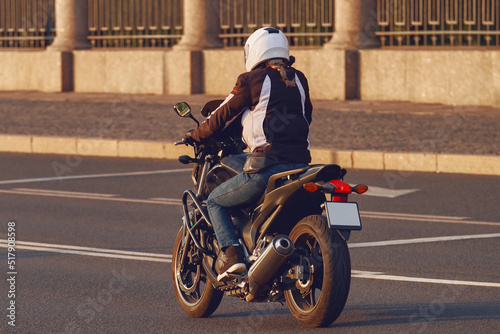 A girl in a helmet rides a motorcycle in the evening city. Young woman motorcyclist travels on a motorbike.