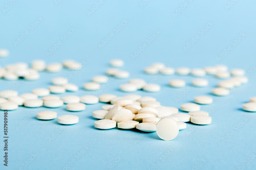 Heap of white pills on colored background. Tablets scattered on a table. Pile of red soft gelatin capsule. Vitamins and dietary supplements concept Heap of white pills on colored background. Tablets scattered on a table. Pile of red soft gelatin capsule. Vitamins and dietary supplements concept