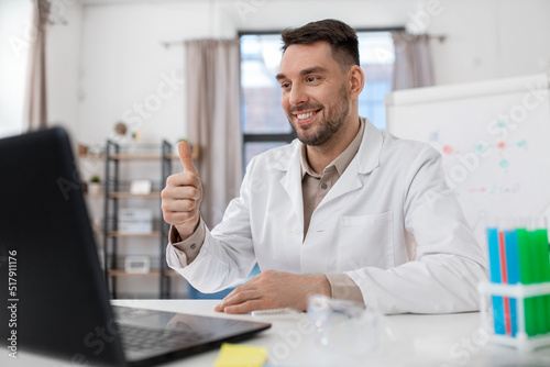 distance education  school and science concept - happy smiling male chemistry teacher with laptop computer having online class and showing thumbs up gesture at home office