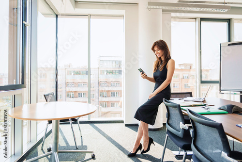 Attractive businesswoman standing in a modern office and using a mobile phone