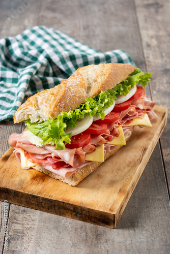 Submarine sandwich with ham, cheese, lettuce, tomatoes,onion, mortadella and sausage on wooden table	