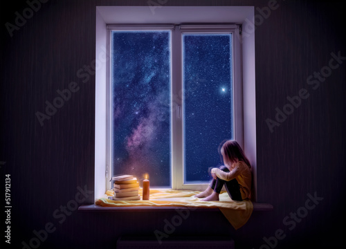 A cute little girl is sitting on the windowsill at night. The child looks at the starry sky. The window shows the sky path and the stars.
