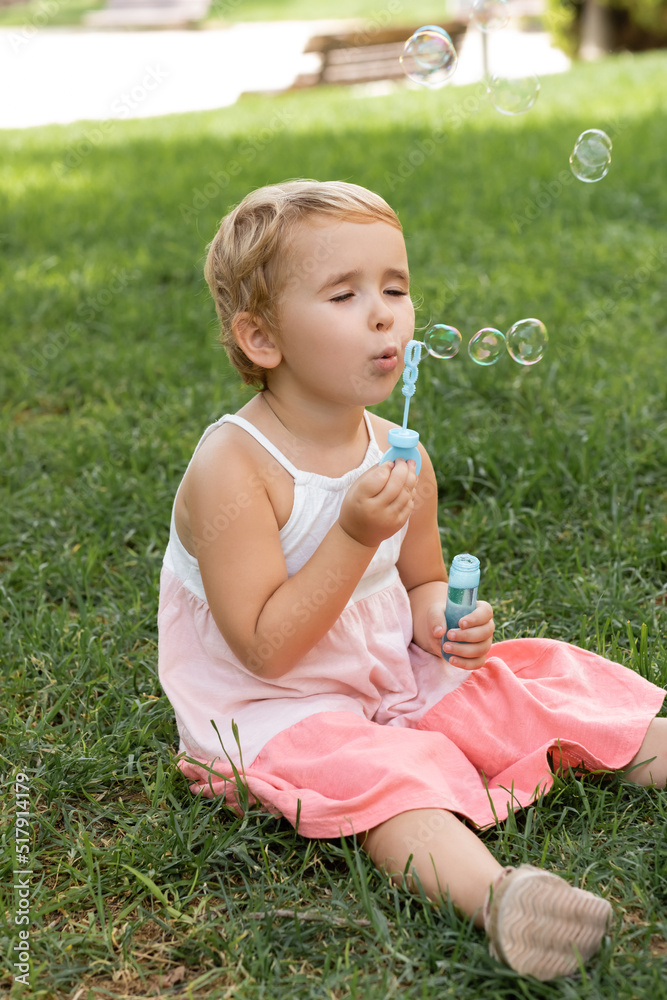 Portrait of toddler kid in dress blowing soap bubbles on lawn. Portrait of toddler kid in dress blowing soap bubbles on lawn.