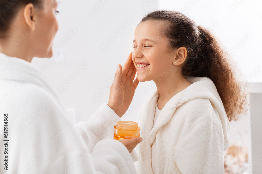 beauty, hygiene, morning and people concept - happy smiling mother and daughter with moisturizer at bathroom beauty, hygiene, morning and people concept - happy smiling mother and daughter with moisturizer at bathroom