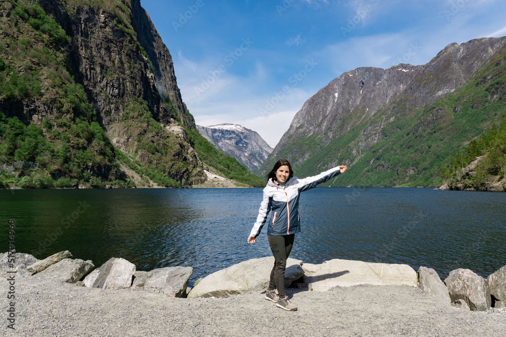 Young tourist woman at the foot of the fjord surrounded by high mountains in Gudvangen - Norway Young tourist woman at the foot of the fjord surrounded by high mountains in Gudvangen - Norway