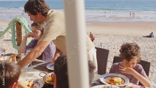 4K SlowMo - family and friends gathered for lunch enjoying a delicious paella in a bar on the beach - happy little kids playing around the table after eating, eating dessert and ice cream