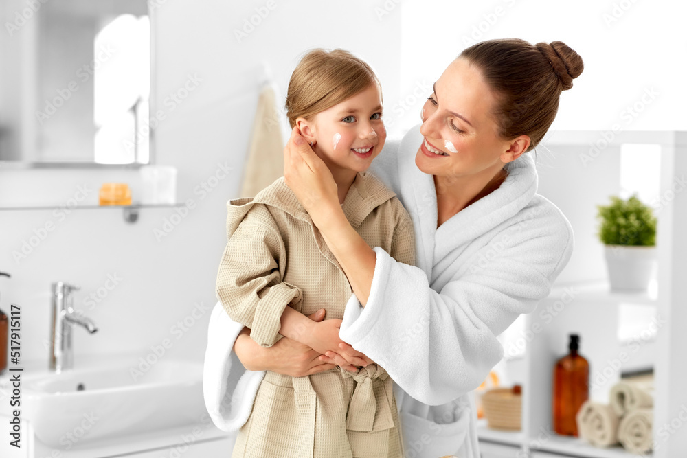 beauty, hygiene and people concept - happy smiling mother and daughter with moisturizer on their faces in bathroom beauty, hygiene and people concept - happy smiling mother and daughter with moisturizer on their faces in bathroom