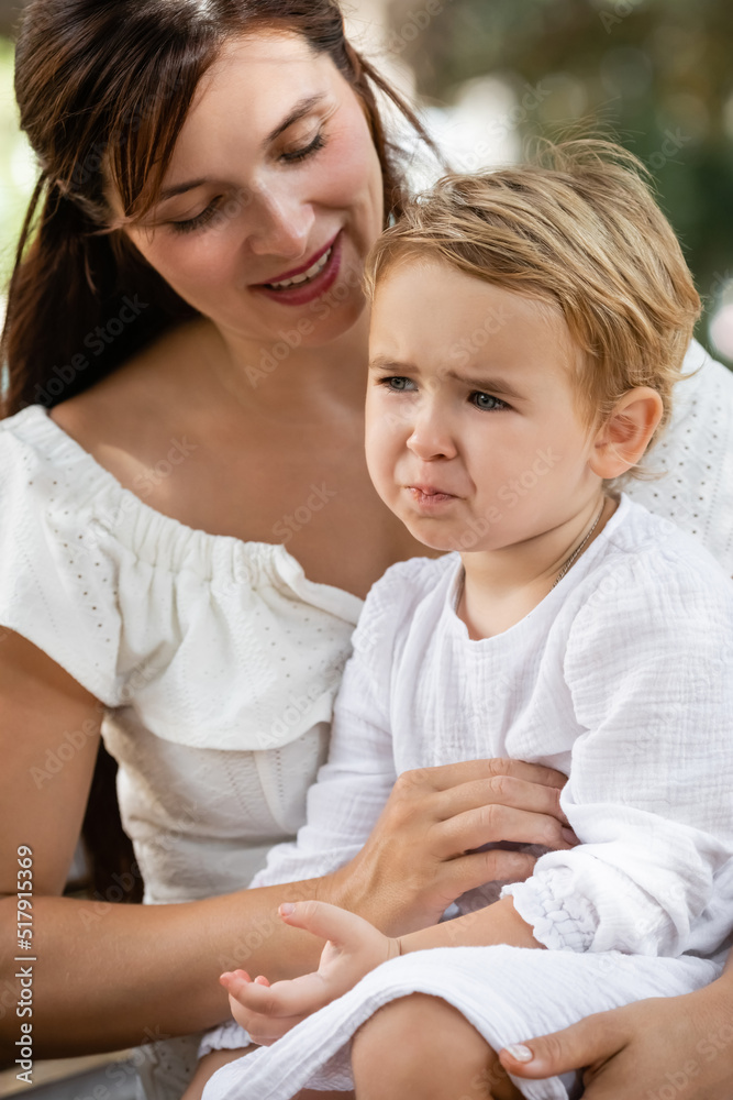Smiling mother looking at sad baby daughter in park.