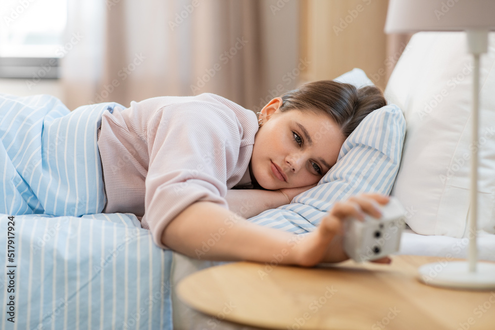 people, bedtime and rest concept - teenage girl looking at alarm clock lying in bed at home in morning people, bedtime and rest concept - teenage girl looking at alarm clock lying in bed at home in morning