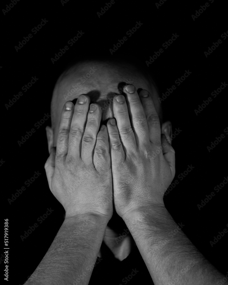 Fototapeta premium a man on a black background covering his face with his hands with one light source