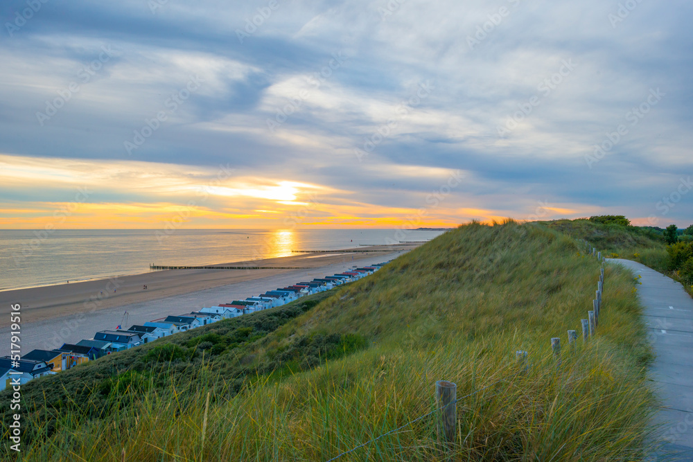 Sand  beach and sand dunes along a sea under a dusk cloudy sky at a bright sunset in summer, Walcheren, Zeeland, the Netherlands, July, 2022