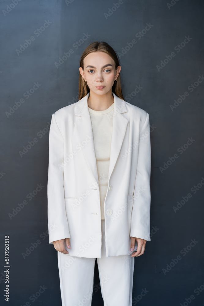 front view of young woman in white blazer looking at camera on black background. front view of young woman in white blazer looking at camera on black background.