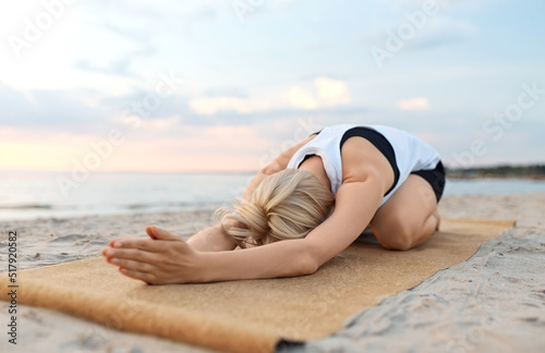 fitness, sport, and healthy lifestyle concept - woman doing yoga child pose on beach over sunset
