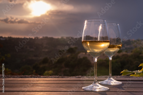 Two elegant glasses of white wine on a table with countryside in the background, at sunset